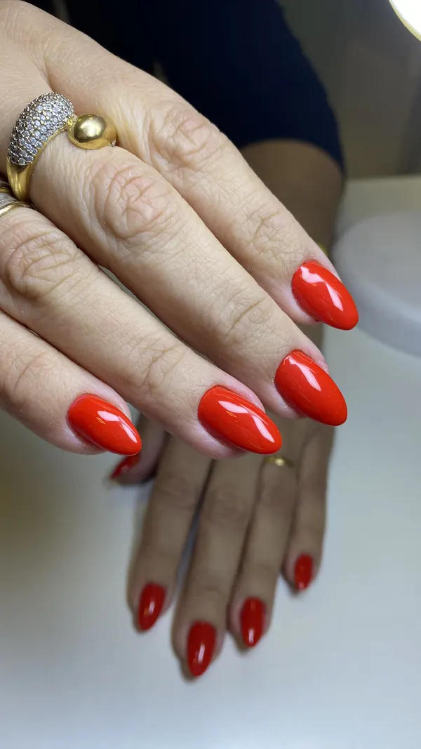 Duas mãos com unhas amendoadas em vermelho coral